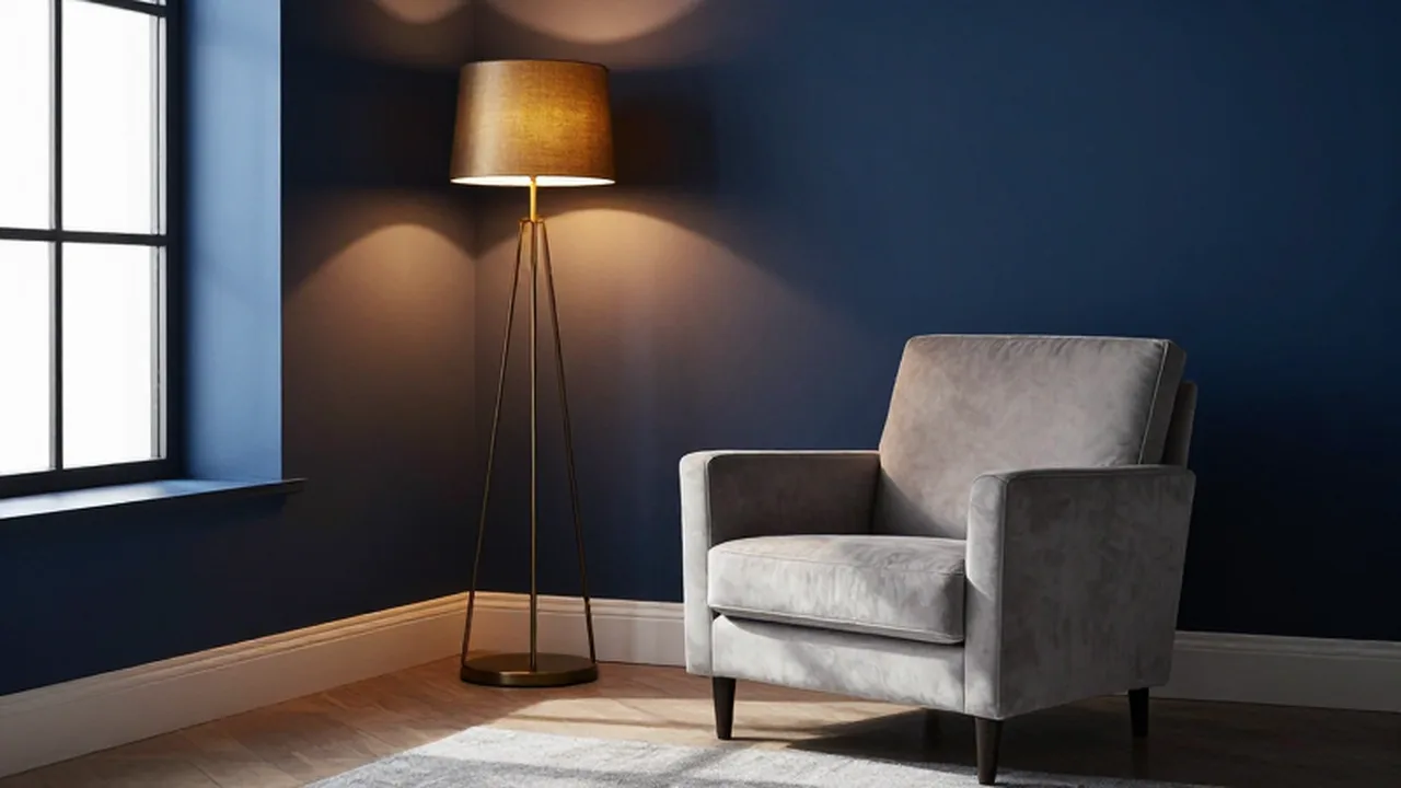 Sillón de terciopelo gris frente a una pared azul marino iluminada por luz cálida.